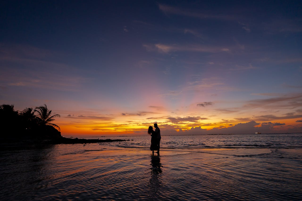 🌸 La decoración ideal para una boda en la playa sencilla No necesitáis grandes arreglos: la playa ya os regala luz y paisaje. Pensad la decoración como acentos que acompañan, no que compitan con el mar. Aquí tenéis ideas concretas (fáciles de montar y con mucho encanto): Arco o telón sencillo: un arco de madera natural con tela ligera (gasa o lino) que se mueva con la brisa. Añadid un ramillete de flores silvestres a un lado para un toque romántico. Centros de mesa casuales: tablas de madera, jarrones bajos con flores locales, o frascos de cristal con arena y velas. Evitad piezas voluminosas que el viento pueda tirar. Iluminación cálida: guirnaldas de luces colgantes para cuando anochezca, farolillos de papel o velas dentro de recipientes cerrados (vasos o latas con arena) para que no se apaguen. Texturas naturales: mantas de lino, alfombras de yute o esterillas para delimitar el espacio; sillas de madera o bancos rústicos. Todo en tonos crudos, verdes y azules suaves. Detalles personales: conchas con los nombres de los invitados como meseros, una pizarra con el seating plan, botellas con mensajes que cuenten anécdotas vuestras. Protección contra el viento y el sol: sombrillas de tela, una pérgola ligera o parasoles; además de prácticos, suman estilo. Plan B para el viento: todo sujeto —cintas pesadas, piedras decorativas en centros, pinzas discretas para las telas— para que nada salga volando. Consejo práctico: elegid proveedores que trabajen con materiales locales y flores de temporada: son más económicos, miran mejor con la brisa y encajan con el espíritu de una boda en la playa sencilla.